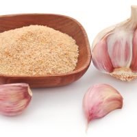 Garlic powder with whole ones over white background