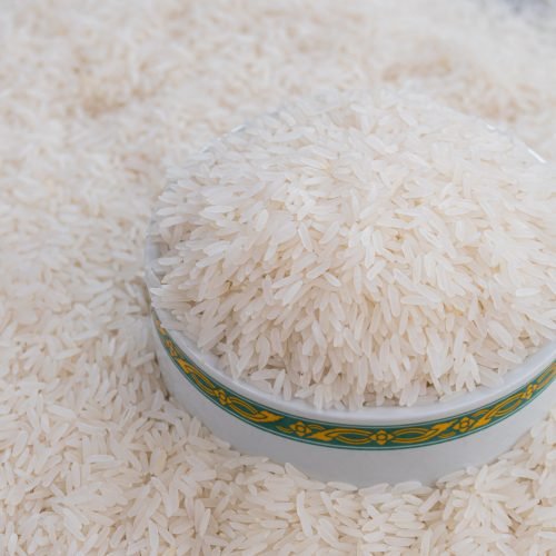 Rice in a white bowl and scattered near on wooden table with copy space for text and design